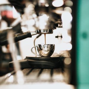 A metal large coffee maker machine pouring coffee into a metal cup